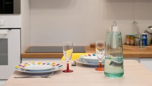 Eine Küche mit einem Holztisch, gedeckt für eine Mahlzeit, mit bunten Tellern, zwei Weingläsern und einer Wasserflasche.