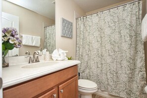 Un baño con lavamanos blanco, tocador de madera y un inodoro. Hay una cortina de ducha con estampado floral.