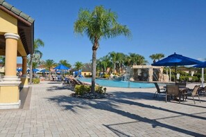 Zona de piscina con palmeras, sillas de descanso y sombrillas.