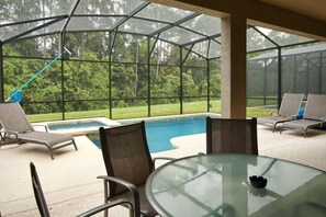 Un espacio al aire libre con paredes de vidrio, una piscina, sillas de descanso y una mesa.