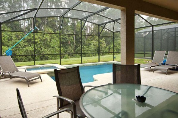 Un espace extérieur abrité par des parois de verre, comprenant une piscine, des chaises longues et une table.