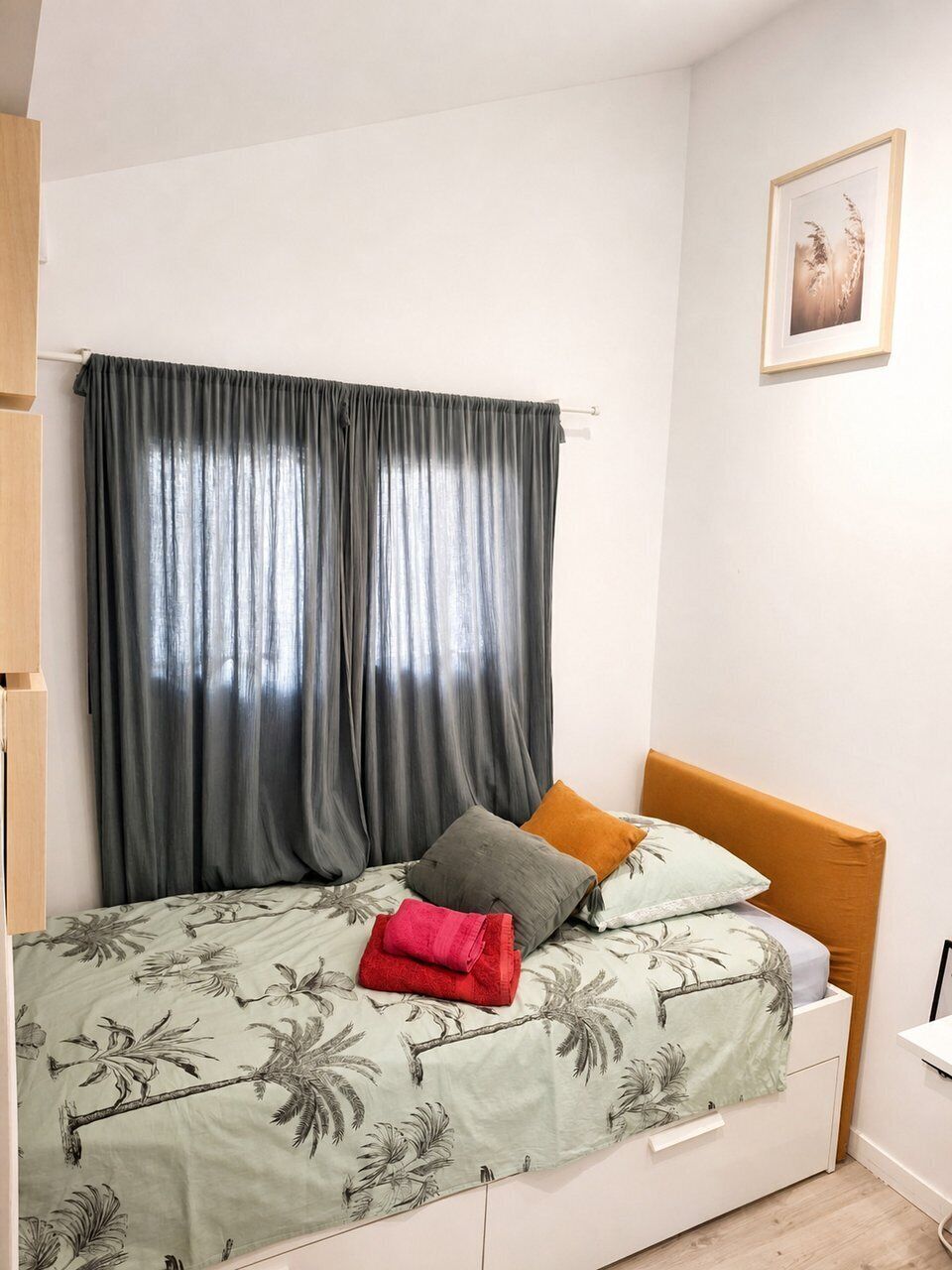 A bedroom with a bed, a nightstand, a drawer, a framed picture on the wall, and a window with curtains.