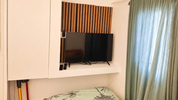 Quarto com uma cama, televisão montada e cortina.