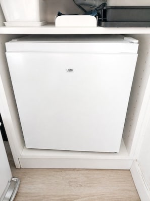 Un miniibar blanco con una etiqueta, ubicado en un rincón de una habitación con piso de madera.