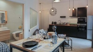 A modern kitchen with a dining area, featuring a large clock, pendant lights, and a refrigerator. - Beautiful atypical apartment AC / garage (Lyon)
