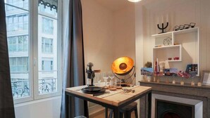 A cozy room with a dining table set for two, a fireplace, and a window with a view of buildings. - Beautiful atypical apartment AC / garage (Lyon)