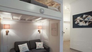 A compact living space with a sofa, two pillows, a wall-mounted lamp, and a geometric artwork.