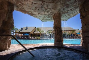 A hot tub area with a pool and a building in the background. - Paradise Palms-4 Bed Townhome W/spashpool-3015pp 4 Bedroom Townhouse by RedAwning (Kissimmee)