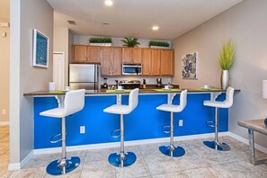 Une cuisine moderne avec un mur d’accent bleu, des appareils en acier inoxydable, des armoires en bois et un coin bar doté de tabourets blancs.