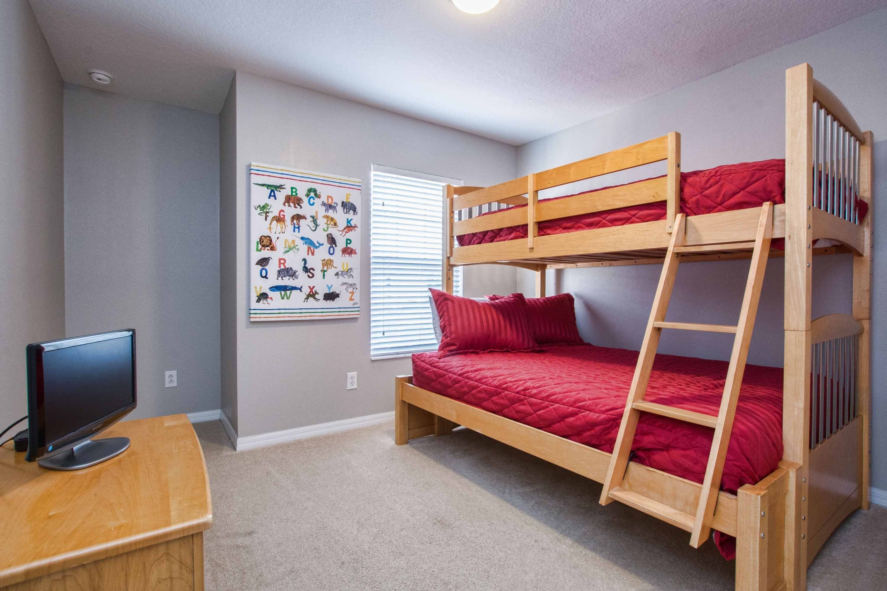A bunk bed with a ladder, a desk with a computer, and a wall with a children's alphabet chart.
