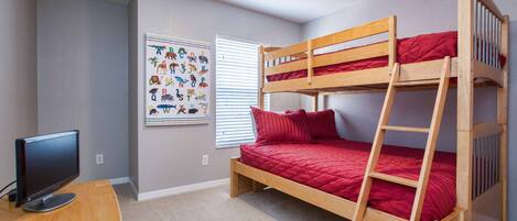 A bunk bed with a ladder, a desk with a computer, and a wall with a children's alphabet chart.