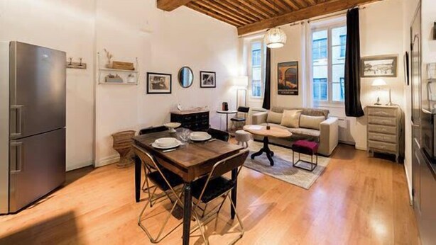A compact kitchen with a dining area, wooden ceiling beams, and a sofa in the living space.