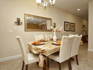 A dining room with a table set for four, chairs, a chandelier, a mirror, and wall-mounted sconces. - Paradise Palms- 4 Bed Townhome W/splashpool-3202pp 4 Bedroom Townhouse by RedAwning (Kissimmee)