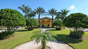 A courtyard with a paved walkway, palm trees, and a building with a yellow facade and arched entrance. - Paradise Palms- 4 Bed Townhome W/splashpool-3202pp 4 Bedroom Townhouse by RedAwning (Kissimmee)