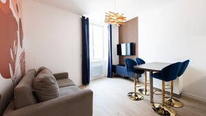 Een moderne woonkamer met een bank, een eettafel met stoelen, een televisie en een opvallende hanglamp.