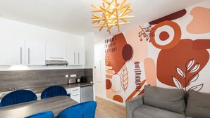 Een moderne keuken met witte kasten, een houten aanrecht en een ingebouwde oven. Er is een eethoek met een houten tafel en blauwe stoelen.