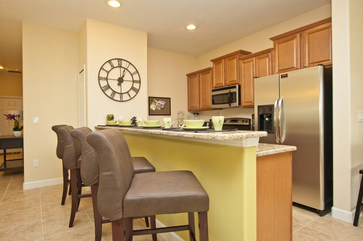 A kitchen with wooden cabinets, a stainless steel refrigerator, a microwave, and a clock on the wall.