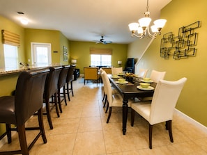 Uma sala de jantar com uma mesa comprida, cadeiras e um lustre.