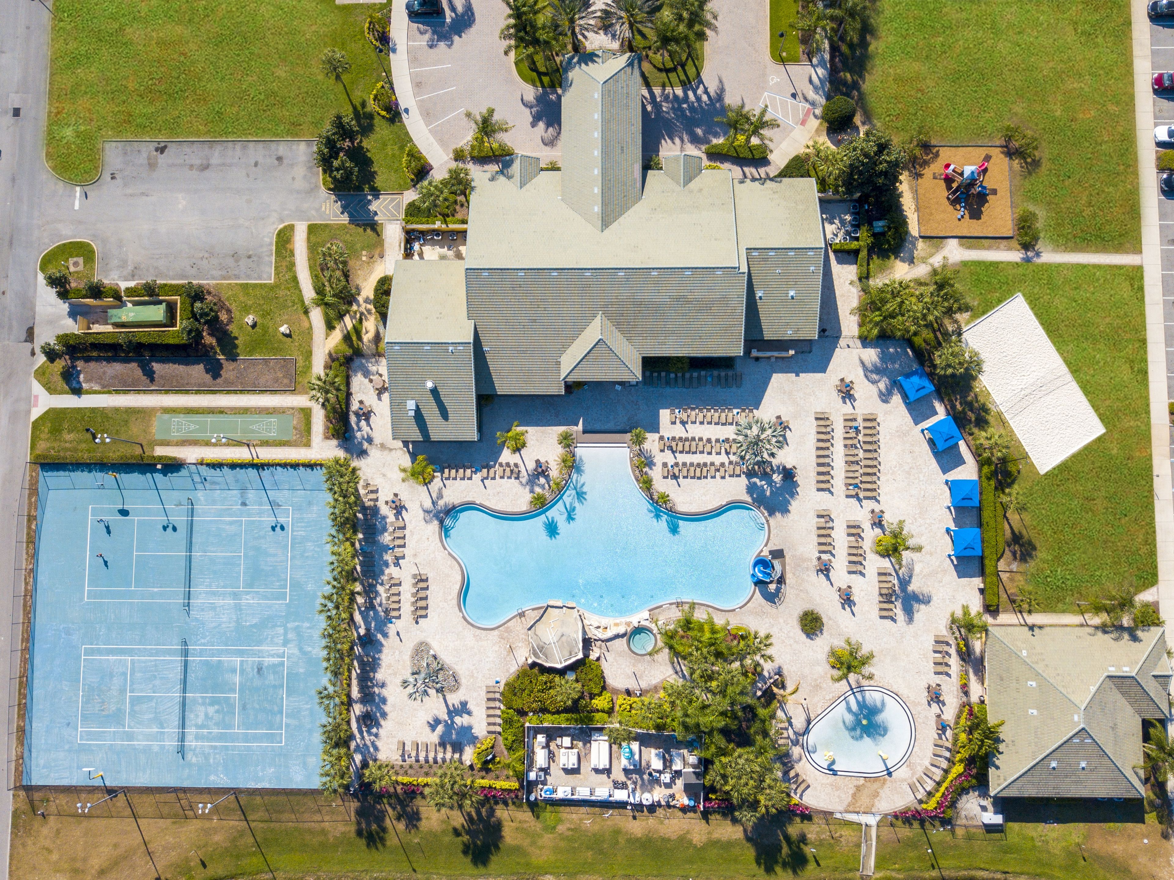 An aerial view of a resort with a large swimming pool, tennis courts, and a clubhouse.