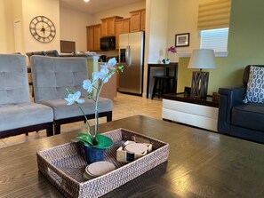A living room with a sofa, a coffee table with a plant and decorative items, a kitchen in the background, and a dining area. - Paradise Palms- 5 Bed Townhome W/splashpool-3024 5 Bedroom Townhouse by RedAwning (Kissimmee)