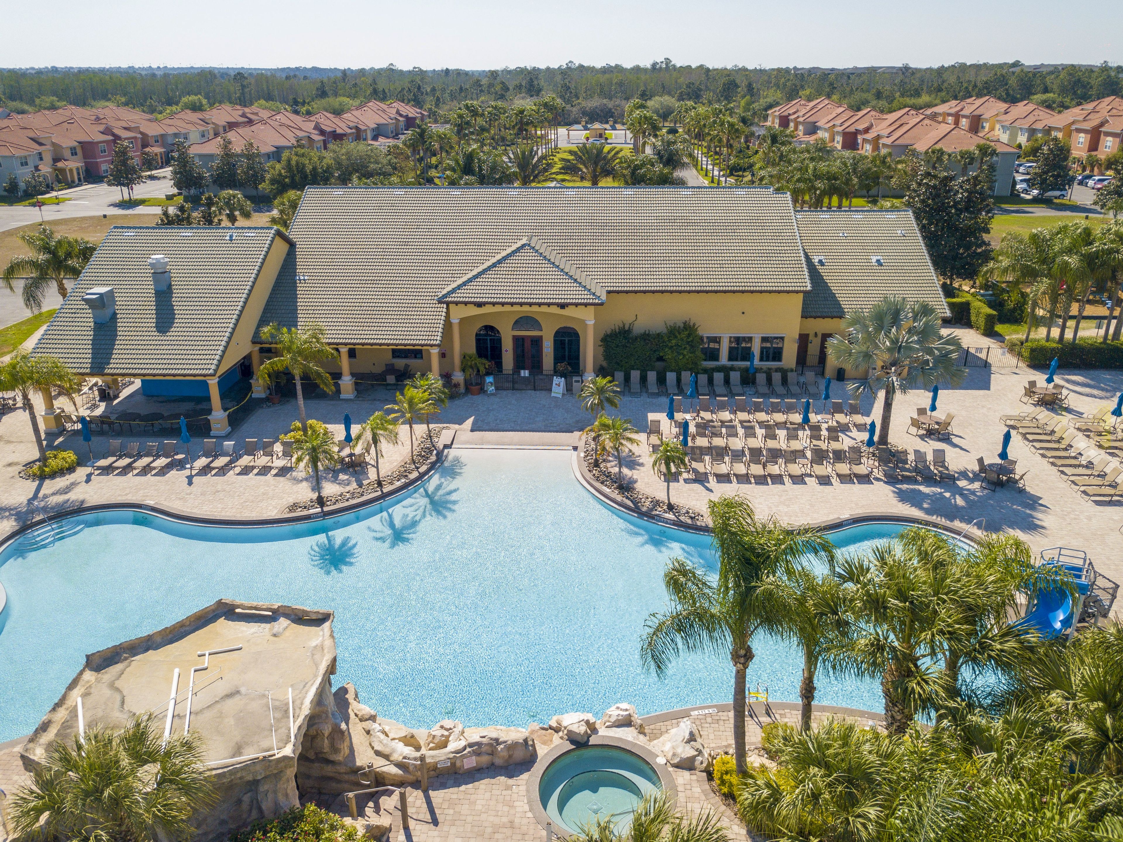 A resort with a large pool, lounge chairs, and a building with a tiled roof.
