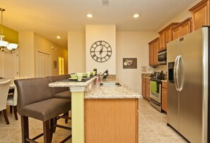 A modern kitchen with a central island, stainless steel appliances, and a wall-mounted clock. - Paradise Palms- 5 Bed Townhome W/splashpool-3024 5 Bedroom Townhouse by RedAwning (Kissimmee)