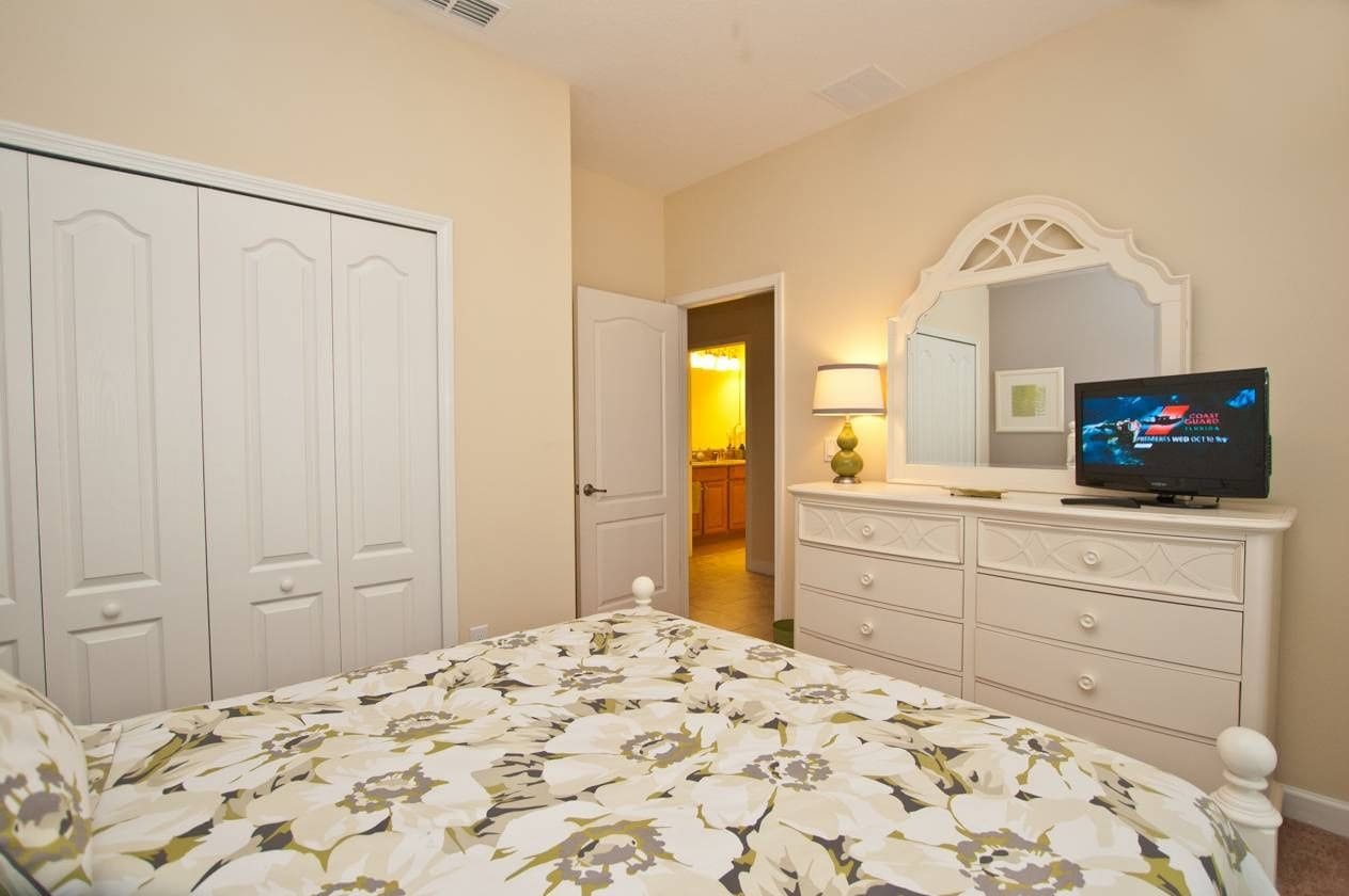 A bedroom with a bed, a dresser, a television, and a door leading to a bathroom.