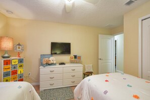 Quarto com duas camas, penteadeira, televisão e porta.