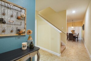 A hallway with a staircase leading to a dining area, a wall-mounted display with numbered hooks, and a vase with a flower on a table. - Paradise Palms-4 Bed W/splashpool-3622pp 4 Bedroom Townhouse by RedAwning (Kissimmee)