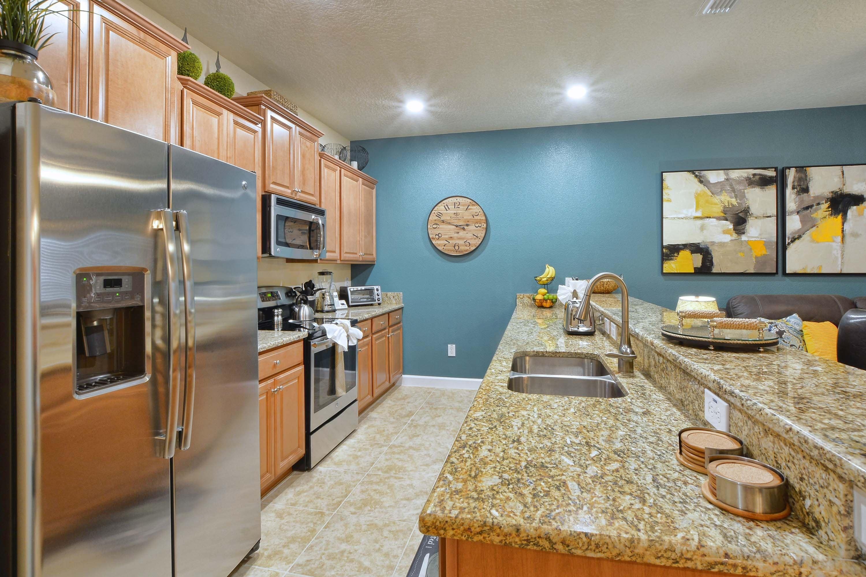 A modern kitchen with stainless steel appliances, wooden cabinets, a granite countertop, and a blue accent wall.