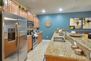A modern kitchen with stainless steel appliances, wooden cabinets, a granite countertop, and a blue accent wall. - Paradise Palms-4 Bed W/splashpool-3622pp 4 Bedroom Townhouse by RedAwning (Kissimmee)