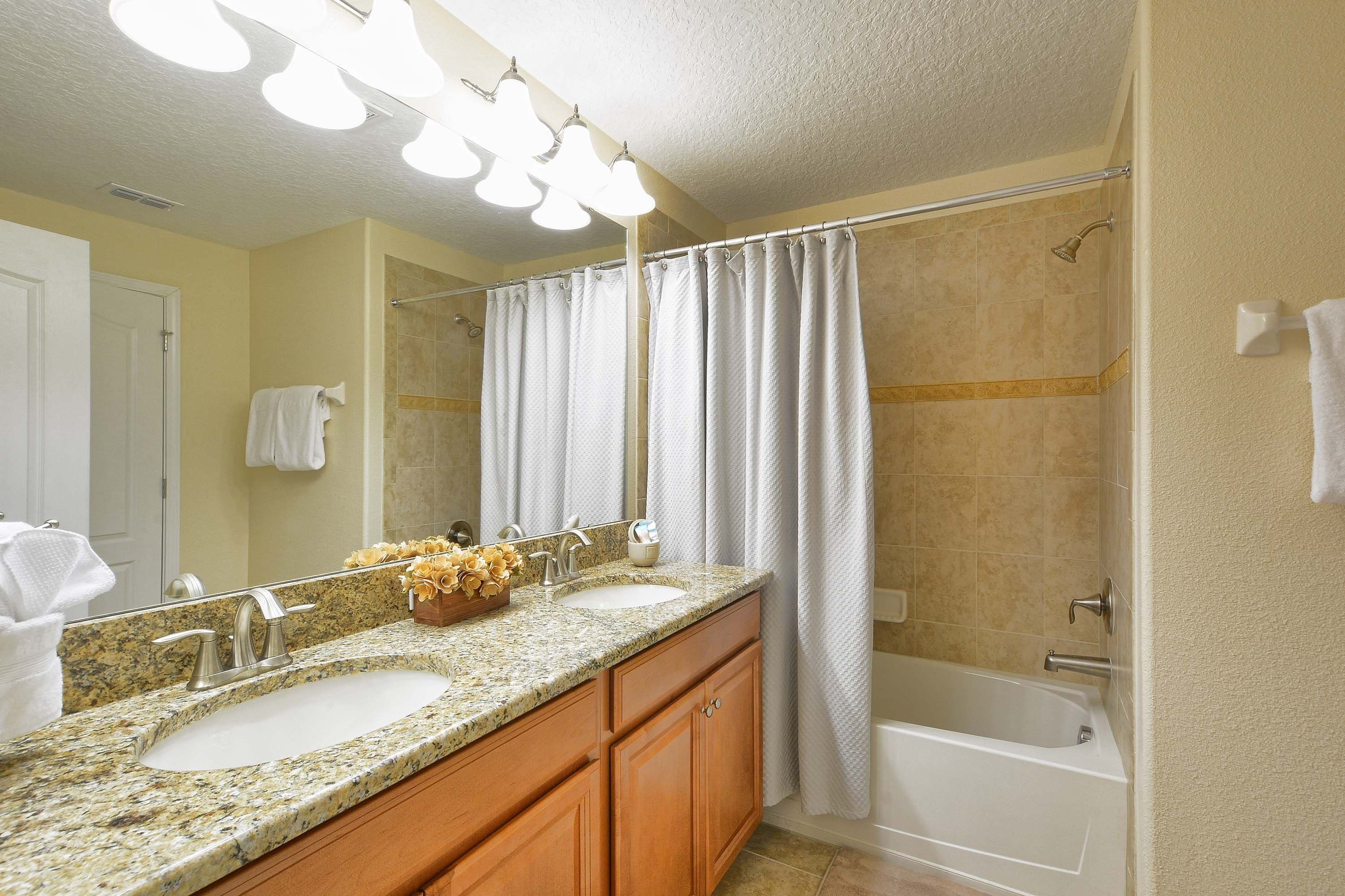 Un baño con lavamanos doble, cortina de ducha, bañera y espejo con luces arriba.
