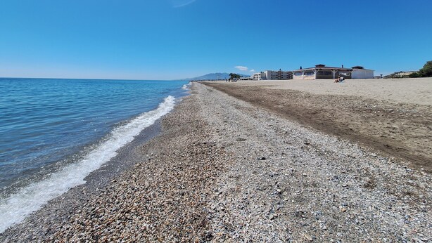 A pebbled beach with a clear sky, a few buildings in the distance, and calm sea. - FH - Holiday rental near the beach in Vera Playa (Vera playa)