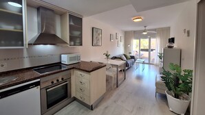 A modern kitchen with a microwave, stove, and cabinets. There is a dining area with a table and chairs, and a living room with a sofa and a plant. - FH - Holiday rental near the beach in Vera Playa (Vera playa)