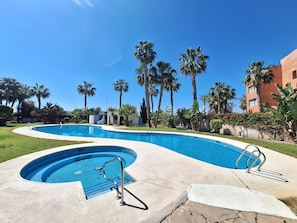 A swimming pool with a curved design, surrounded by palm trees and a building in the background. - FH - Holiday rental near the beach in Vera Playa (Vera playa)