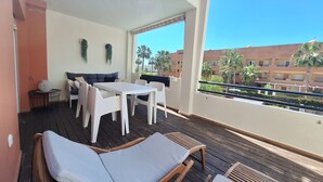 A balcony with a wooden deck, white furniture, and a view of palm trees and buildings. - FH - Holiday rental near the beach in Vera Playa (Vera playa)