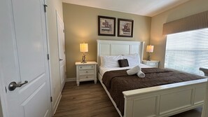 A bedroom with a bed, two bedside tables with lamps, a door, and a window with blinds.