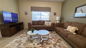 A living room with a brown leather sofa, a glass coffee table, a television on a wooden stand, and a patterned rug.