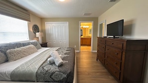 A bedroom with a bed, dresser, television, and a hallway leading to a bathroom.