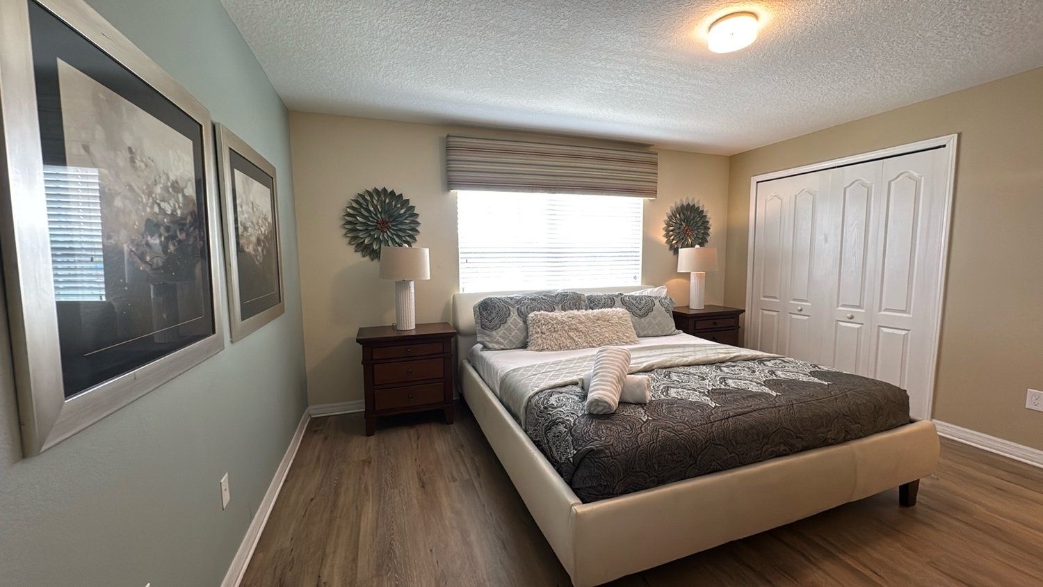 Une chambre à coucher comprenant un lit, des tables de chevet, une fenêtre avec des stores et une armoire.