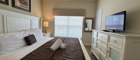 A hotel room with a bed, a television, a dresser, and a window with blinds.