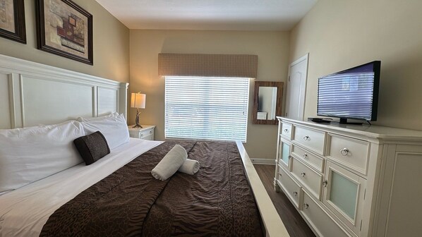 Habitación de hotel con una cama, televisor, cómoda y ventana con persianas.