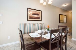 A dining area with a wooden table set for four, a striped sofa, and a framed picture on the wall. - Paradise Palms- 4 Bed Townhome W/splashpool-3044pp 4 Bedroom Townhouse by RedAwning (Kissimmee)