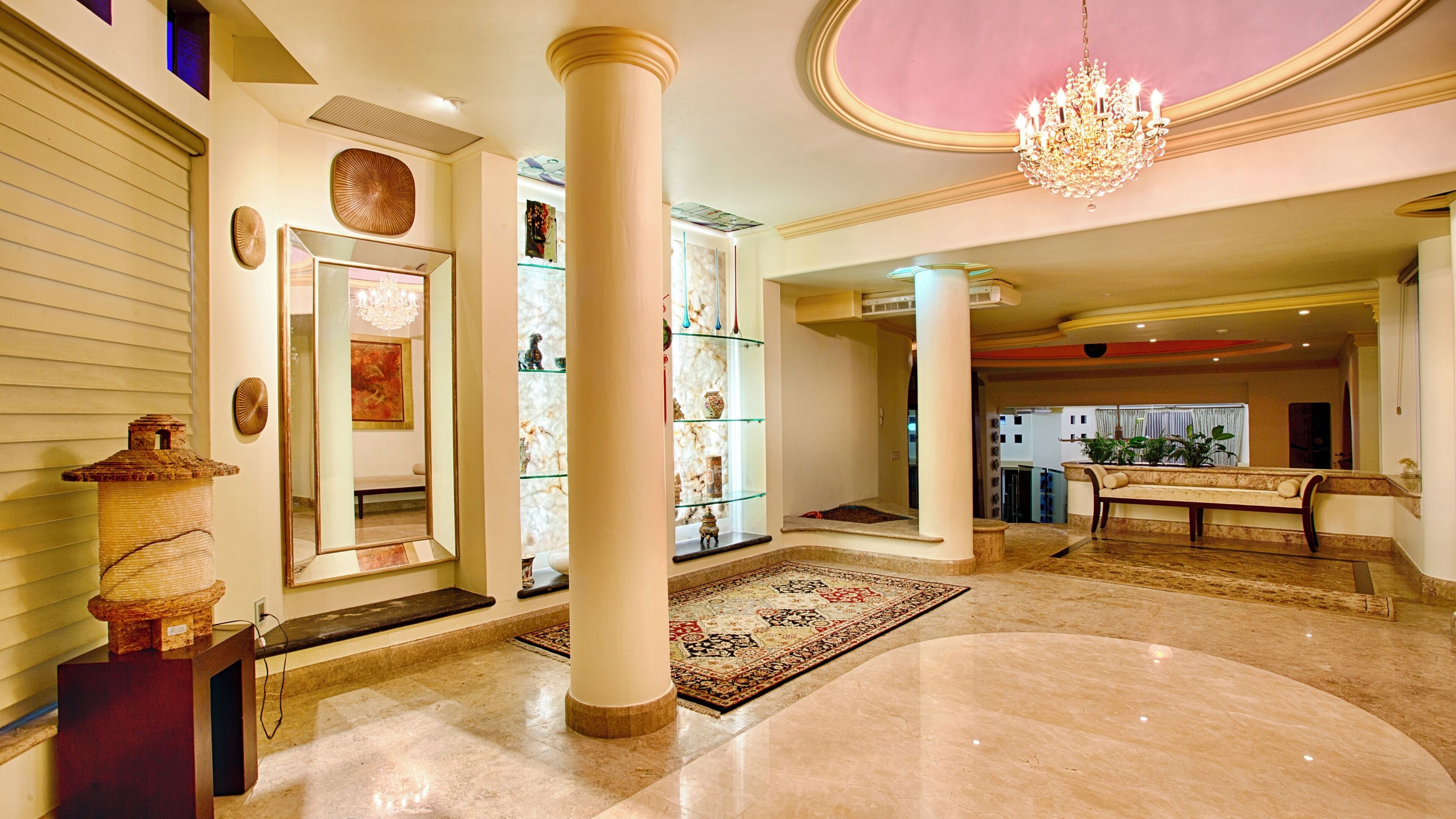 A spacious lobby with marble flooring, a grand chandelier, and a seating area with a bench.