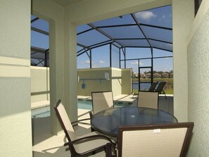 Ein überdachter Außenbereich mit Sitzgelegenheiten, Blick auf den Pool, Stühle und ein Tisch.