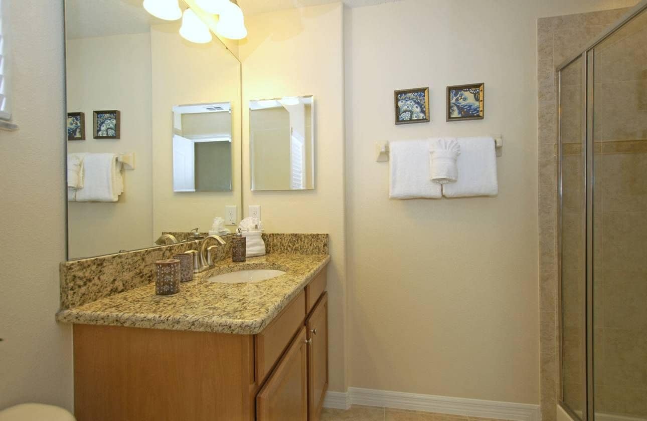 A bathroom with a granite countertop, two sinks, a large mirror, and a glass shower enclosure.