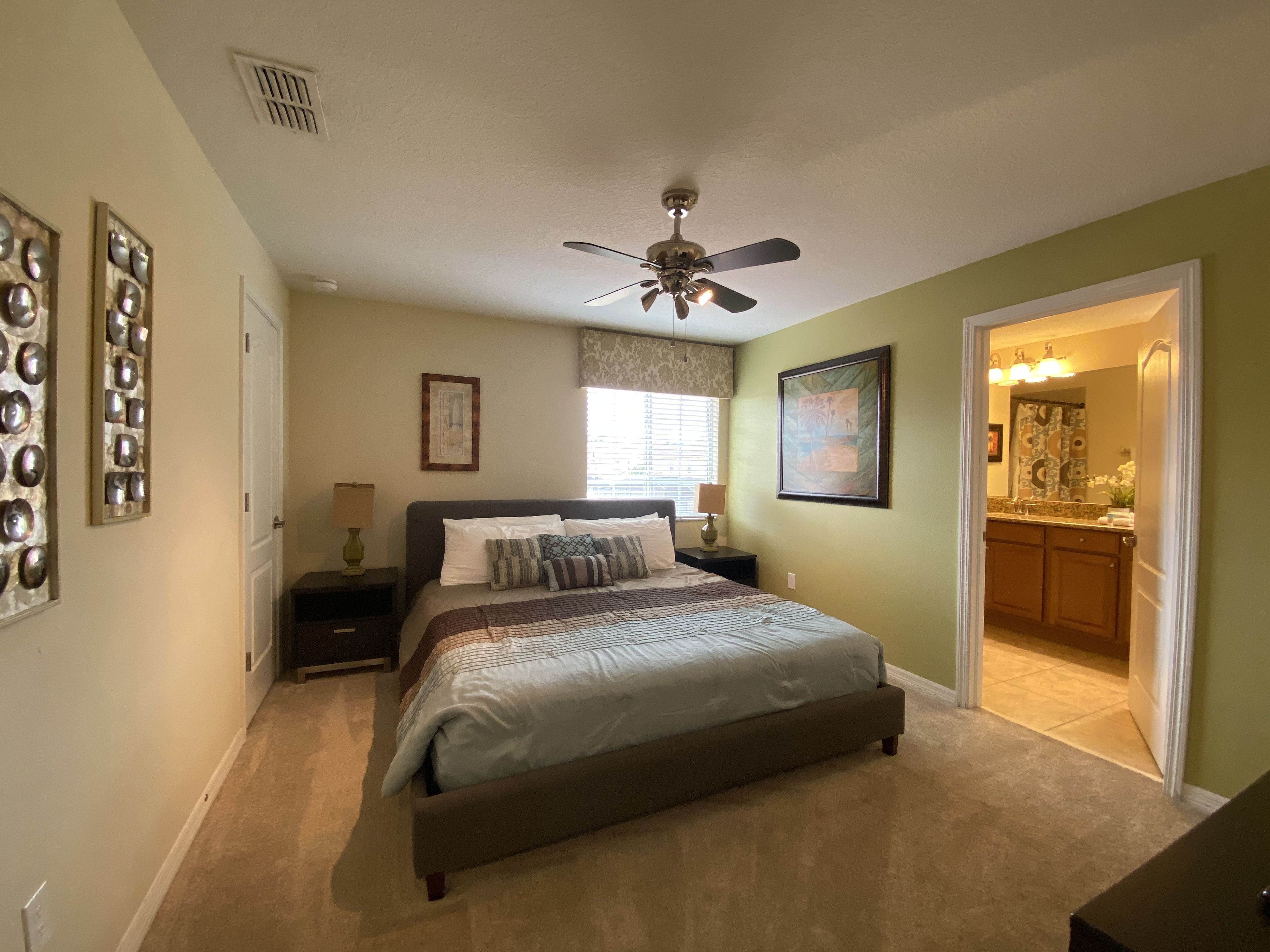 A bedroom with a bed, nightstands, a ceiling fan, and a bathroom visible through an open door.