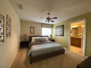 A bedroom with a bed, nightstands, a ceiling fan, and a bathroom visible through an open door. - Paradise Palms- 5 Bed Townhome W/splashpool-3020pp 5 Bedroom Townhouse by RedAwning (Kissimmee)