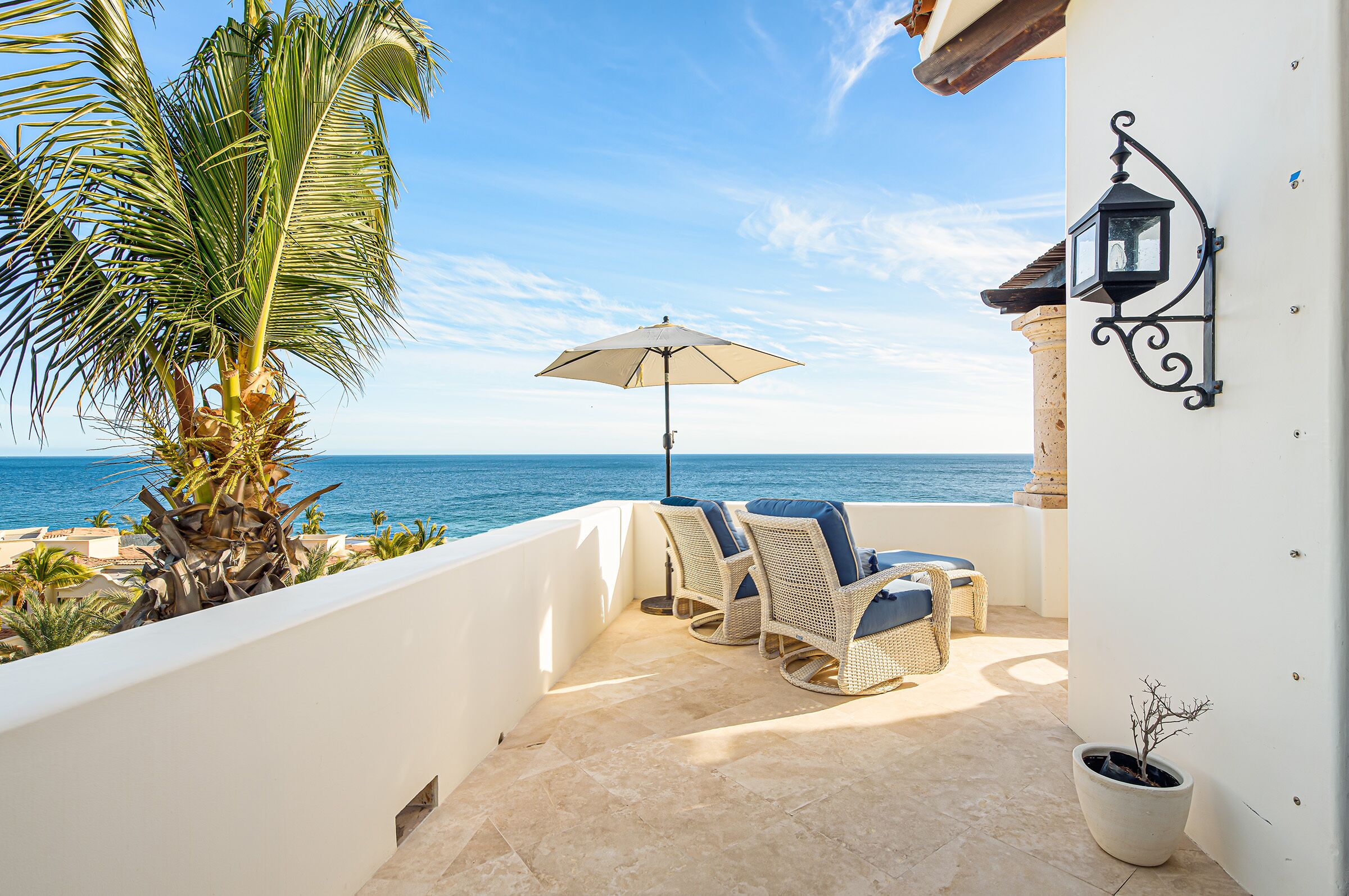 Een balkon met rieten meubilair, een potplant en uitzicht op zee.