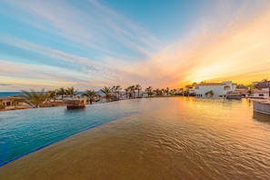 A resort pool with a sunset view, palm trees, and buildings in the background.